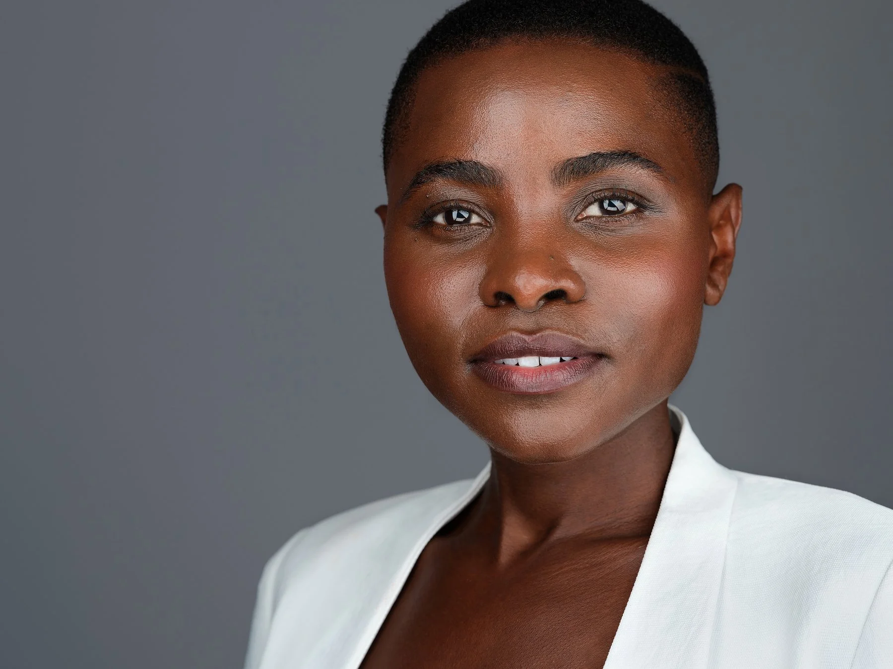 Close-up portrait of an African American woman with short hair wearing a white blazer against a gray background.