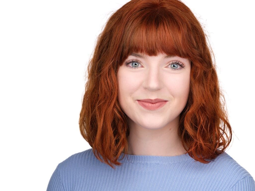 LinkedIn headshot of a woman with red hair in a blue top, natural expression, Toronto studio