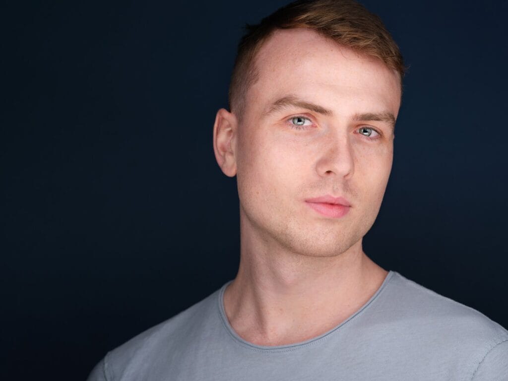 Actor headshot of a young man in a grey shirt against a deep navy background, Toronto studio