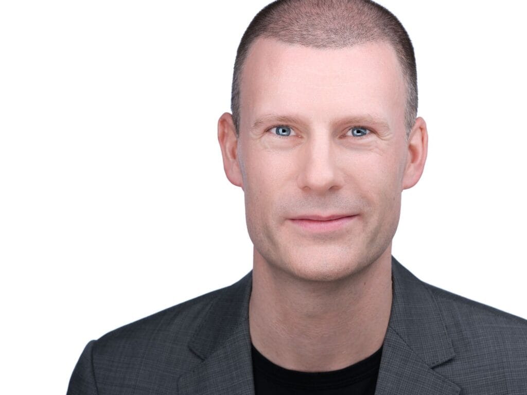 Business headshot of a man in a grey suit jacket over a black t-shirt on a white background, Toronto studio