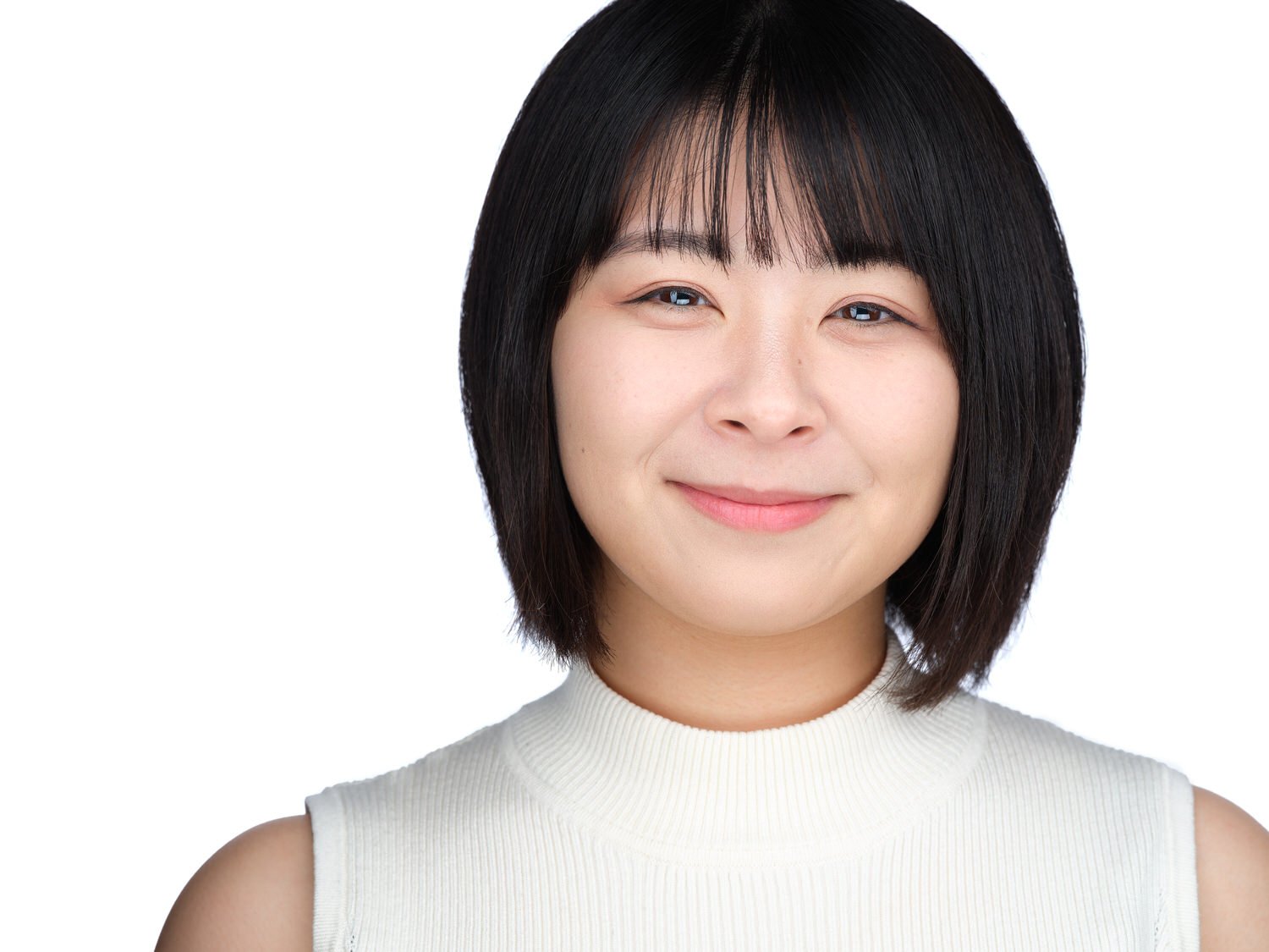 Close-up of a young woman with short black hair, wearing a sleeveless white top, smiling softly against a white background.