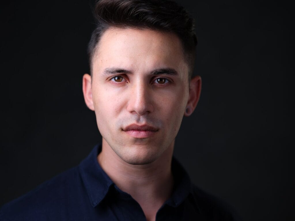 Theatrical actor headshot of a man in a dark shirt on a dark background, neutral expression, Toronto studio