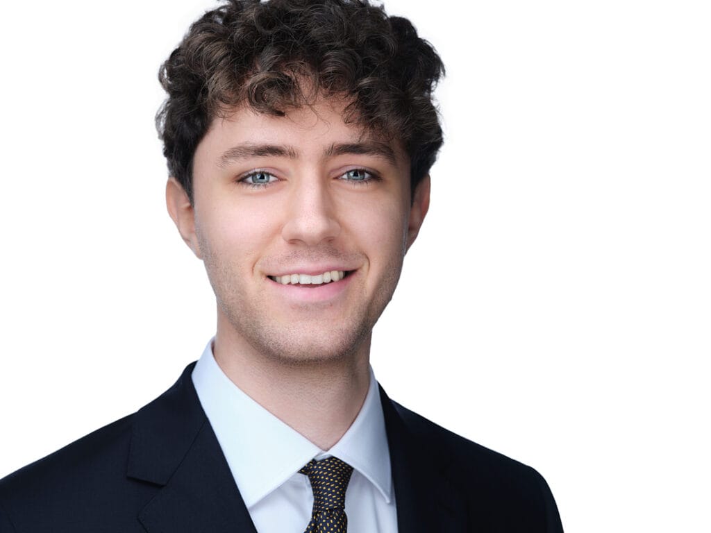 LinkedIn headshot of a man in a navy suit and gold-patterned tie smiling on a white background, Toronto studio session