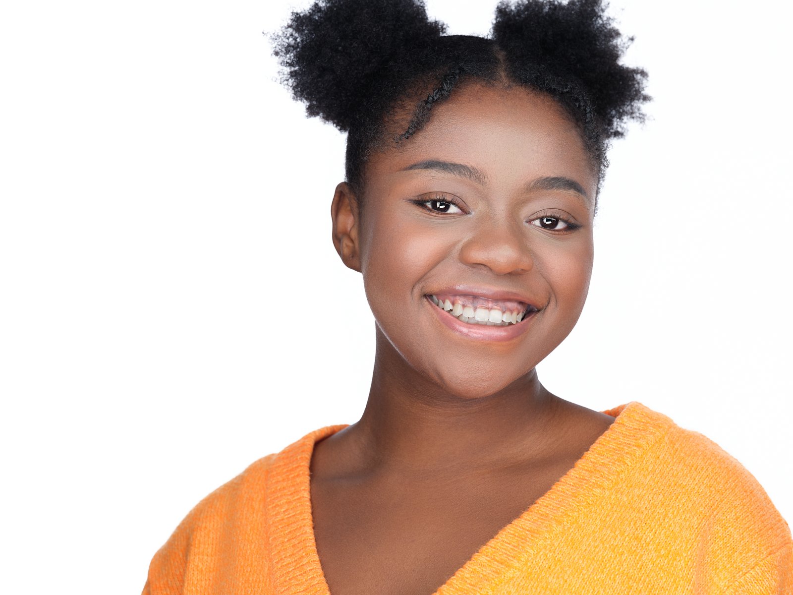 A young woman with natural hair styled in puffs, smiling, wearing an orange top, against a white background.