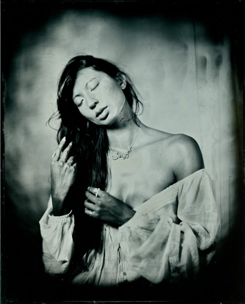 Wet plate collodion tintype portrait of a woman with her eyes closed, gathering her long dark hair, hand-poured 8x10 plate made in Toronto